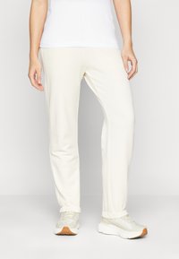 Pantalons de survêtement crème clair en tissu doux avec une coupe fuselée, des poignets côtelés et des poches latérales, associés à des chaussures de sport de couleur claire.