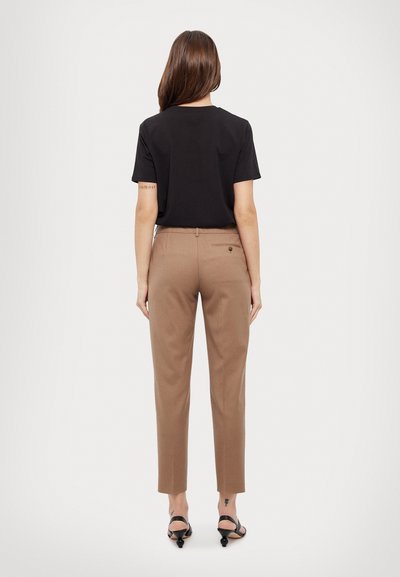 Zwarte korte mouwen t-shirt gecombineerd met bruine op maat gemaakte broek. De broek heeft een achterzak en knoopdetails, gedragen met zwarte strappy hakken.