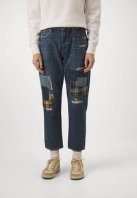 Denimjeans med en mörkblå tvätt, med patchworkdetaljer i rutigt och olika denimtexturer, slitna områden och en avslappnad passform.