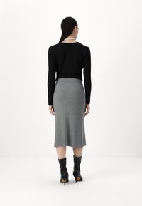 Svart långärmad topp, åtsittande vid midjan. Grå ribbad midiklänning, avsmalnande form med en sidoklyfta. Knähöga svarta klackstövlar.