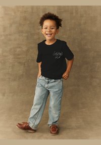 Black short-sleeve t-shirt with white graphic design on the chest, paired with light blue loose-fitting jeans and brown shoes.