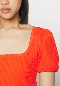 Top de mangas curtas em tecido canelado laranja brilhante, com decote quadrado e mangas bufantes com um acabamento texturizado.