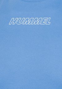 Blue t-shirt with a textured fabric, featuring the word "HUMMEL" in bold white letters across the chest. Round neckline.