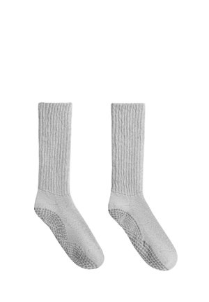 Paire de chaussettes hautes gris clair avec texture côtelée et grips antidérapants sous la semelle, affichées côte à côte sur un fond blanc.