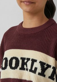 Bordeaux gebreide trui met ribbelstructuur en een crèmekleurige streep met het woord "BROOKLYN" in dikke zwarte letters.