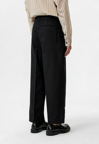 Zwarte broek met brede pijpen, gemaakt van duurzaam materiaal en met een gladde afwerking. De achterkant heeft een eenvoudig ontwerp met een verborgen zak.