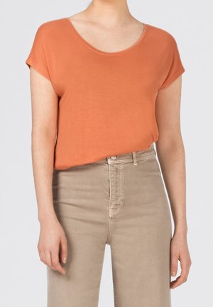 Oranje T-shirt met korte mouwen en een brede ronde hals, gecombineerd met lichtbeige, hooggesneden jeans, gladde stof, minimalistisch ontwerp.