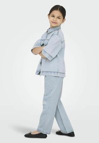 Ljusblå denimjacka med kort ärm och framficka, kombinerad med ljusblå revade jeans och svarta baletttofflor.