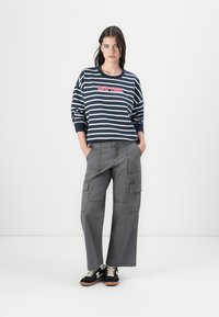 Marineblå og hvite stripete bomullssweatshirt med "NEW YORK" trykket i rødt, kombinert med grå cargo-bukser med flere lommer og vide ben.
