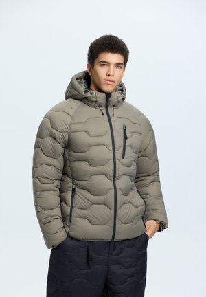 Veste matelassée en vert olive avec capuche, présentant un design matelassé et des zippers noirs. Équipée de poches zippées sur les côtés et la poitrine.