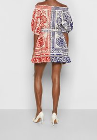 Vestido off-shoulder con mangas abullonadas, con un patrón floral en rojo, azul y blanco. Dobladillo con volantes y cintura ceñida. Tacones blancos.