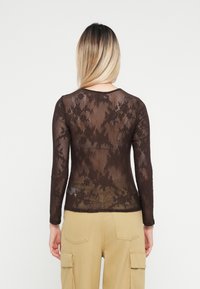 Top marrone a maniche lunghe realizzato in pizzo leggero con un motivo floreale; scollatura rotonda e design aderente, abbinato a pantaloni cargo beige.