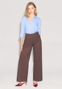 Camicia azzurra chiaro con maniche arrotolate; pantaloni larghi marroni; tacchi a punta rossi con cinturini decorativi.