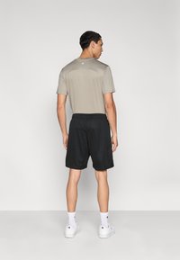 Ανδρική αθλητική εμφάνιση με ανοιχτό γκρι κοντομάνικο πουκάμισο και μαύρα σορτς από δίχτυ. Το λευκό αθλητικό παπούτσι και οι κάλτσες ολοκληρώνουν την εμφάνιση.