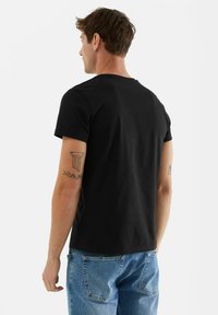 Svart bomullströja med rund hals, korta ärmar och avslappnad passform, som är kombinerad med ljusblå jeans.