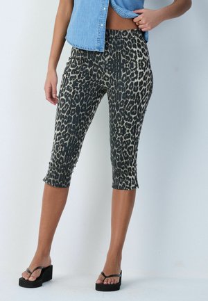 Mujer con pantalones cortos de estampado de leopardo, camisa sin mangas de mezclilla y sandalias negras con plataforma sobre un fondo claro y liso.