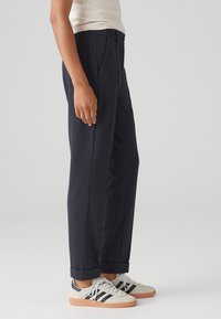 Skräddarsydda mörkblå byxor med rak bendesign, med framfåll och uppvikt nederkant. Bärs med avslappnade sneakers.