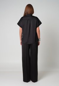 Zwarte satijnen short-sleeve shirt met een ontspannen pasvorm, rugplooidetail, gecombineerd met hoge taille, wijde zwarte broek. Gladde textuur.