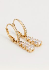 Zlaté kruhové náušnice s čírymi drahokamami. Dolná časť obsahuje tri väčšie kamene a rad menších kameňov pozdĺž kruhu.