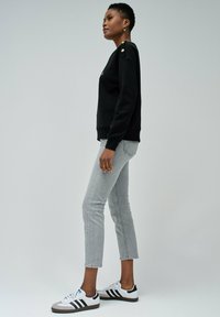 Sweatshirt noir avec des accents de boutons dorés, associé à un jean gris clair et des baskets noir et blanc. Tissu lisse et coupe décontractée.