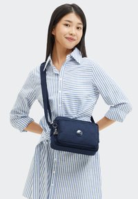 Borsa a tracolla blu navy con texture a coste, dotata di chiusura con bottone in argento, tasca con zip e tracolla regolabile.