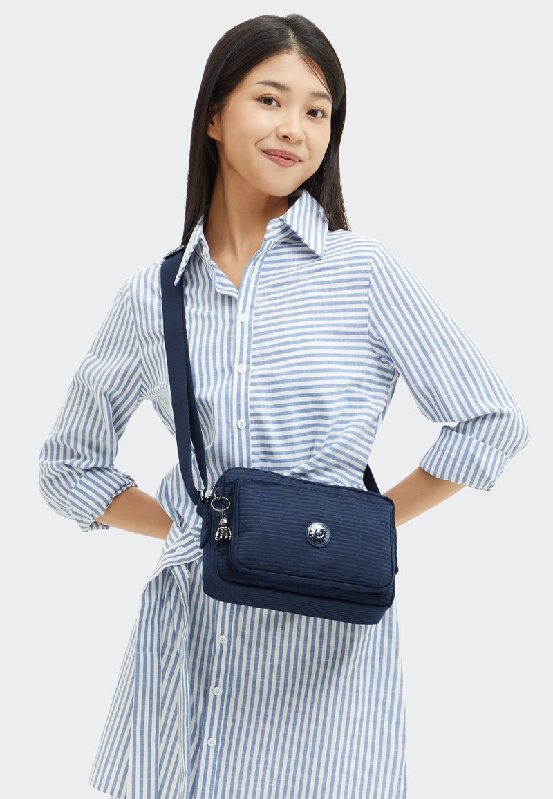 Borsa a tracolla blu navy con texture a coste, dotata di chiusura con bottone in argento, tasca con zip e tracolla regolabile.