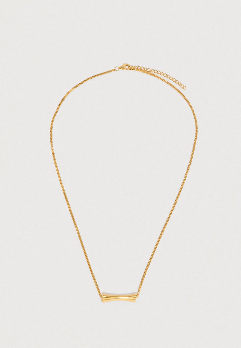 Colar delicado em corrente de ouro com um pendente horizontal liso e ligeiramente curvado, e fecho ajustável, sobre um fundo claro.