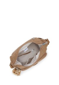 Torebka crossbody Tan Kipling z otwartym głównym zamkiem błyskawicznym, wewnętrzną klipsą na klucze, beżową podszewką oraz małym pluszowym breloczkiem w kształcie małpki przymocowanym na zewnątrz.