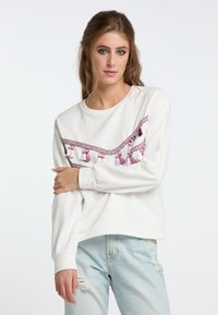 Felpa bianca con dettagli in frange rosa e lavorazione a treccia sul petto. Presenta maniche lunghe e un design dal taglio morbido.
