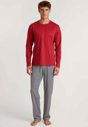 Rode lange mouwen pyjama-top gecombineerd met loszittende, gestreepte broek met een blauw, rood en witte diamantontwerp. Schoeisel niet zichtbaar.