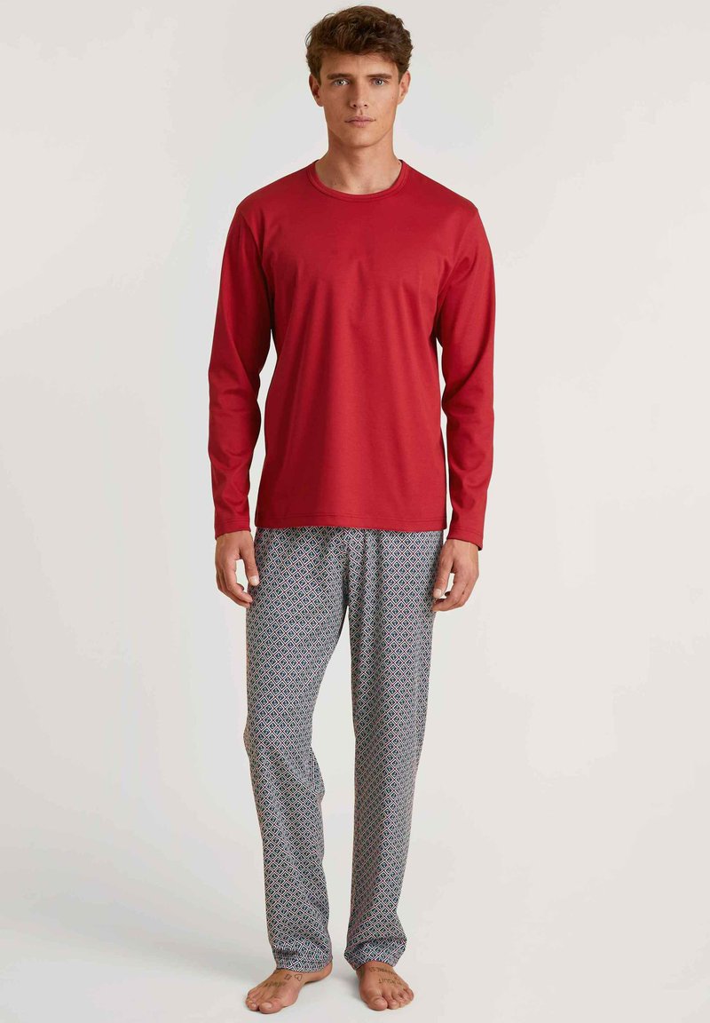 Un haut de pyjama rouge à manches longues associé à un pantalon ample à motifs présentant un design en diamants bleu, rouge et blanc. Chaussures non visibles.