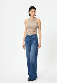 Beige ribbed tank top yhdistettynä vaaleansinisiin leveälahkeisiin farkkuihin. Farkuissa on perinteinen viiden taskun muotoilu ja napitus. Mustat kengät.