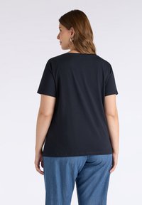 Svart kortärmad T-shirt med rund halsringning, gjord av slät tyg, designad för en avslappnad passform, tillsammans med lösa denimjeans.