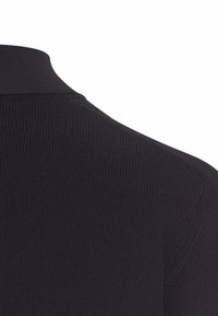 Sort ribbet strikket beklædning med høj krave, der har en tekstureret overflade og en tætsiddende silhuet. Designet til en tæt pasform omkring halsen.