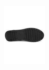 La semelle noire de la chaussure présente un fond en caoutchouc texturé avec des rainures horizontales et un bout arrondi. Le nom de la marque est embossé sur la surface.