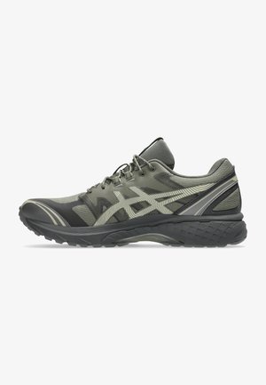 Green athletic shoe with a textured mesh upper, curved design, patterned accents, and a black, rugged sole for traction. Laces for secure fit.
