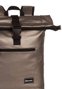 Grauer wasserdichter Rucksack mit Rollverschluss, schwarzem Zubehör und einer Fronttasche mit Reißverschluss. Verfügt über ein Logo-Patch und gepolsterte Schultergurte.