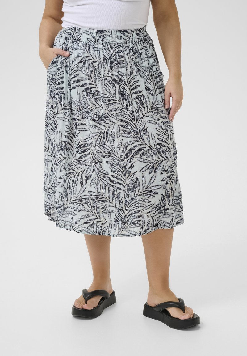 Jupe florale midi de couleur bleu clair, ornée d'un motif de feuilles noires, avec une taille élastique et des poches latérales. Associée à des tongs noires.