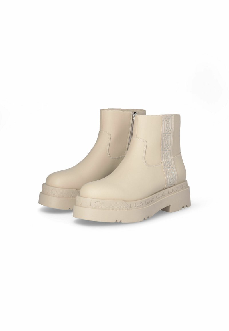 Beige Knöchelstiefel aus glattem Material mit einem seitlichen Reißverschluss, dicker Sohle und geprägtem Logo-Detail auf der Rückseite.