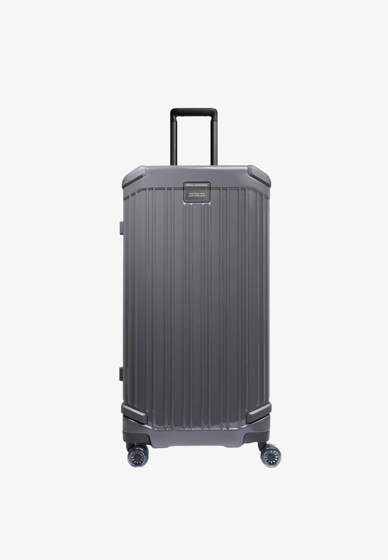 Grauer Rollkoffer mit vertikalen Rillen, einem ausziehbaren Griff, abgerundeten Ecken und strapazierfähigem Kunststoffmaterial. Verfügt über vier Räder für hohe Mobilität.