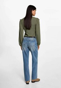 Olivgrön blus med puffärmar, kombinerad med ljusblå raka jeans. Svart bälte med texturerad yta. Bruna ankelskor.