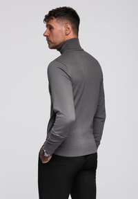 Maglione grigio aderente con collo alto e maniche lunghe, dotato di polsini a coste. Tessuto liscio con un design pulito e minimalista.