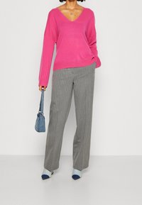 Suéter de pico rosa, pantalones de rayas grises, bolso azul y tacones en bloque de color con detalles en azul claro, azul oscuro y punta afilada.