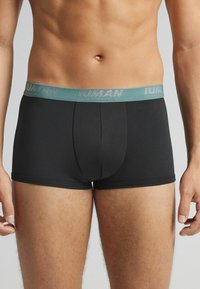 Boxer ajustados negros con una cinturilla turquesa. La cinturilla presenta el texto "HUMAN" en relieve. El material parece suave y tiene un diseño ceñido.