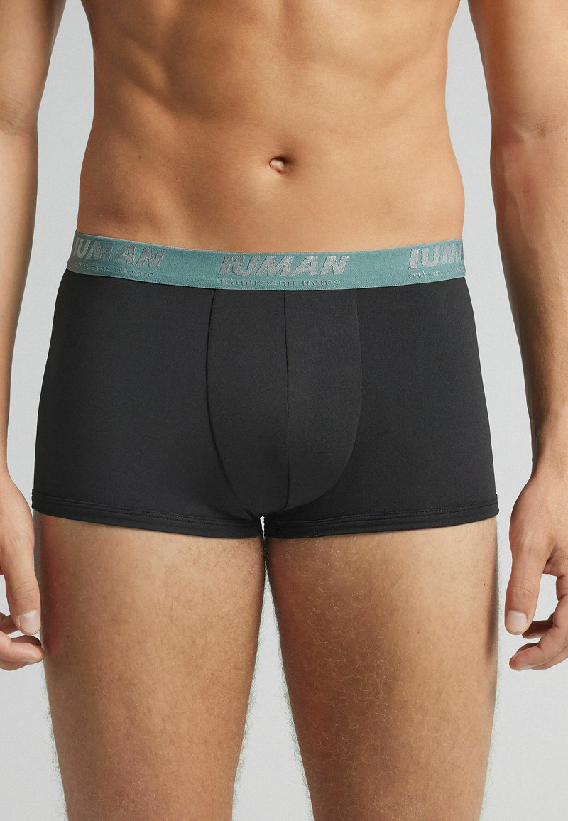 Boxer ajustados negros con una cinturilla turquesa. La cinturilla presenta el texto "HUMAN" en relieve. El material parece suave y tiene un diseño ceñido.