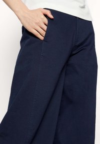 Marina vida byxor med släta bomullstyg. Har sidofickor och en åtsittande midja för komfort och enkel användning.