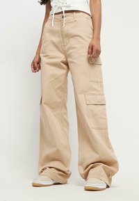 Beige cargobyxor med en lös passform, som har två sidofickor, dragsko i midjan och är gjorda av ett mjukt bomullsmaterial.