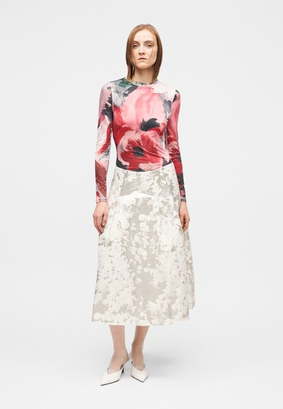 Μπλούζα μακρυμάνικη με λουλούδια σε αποχρώσεις του ροζ και κόκκινου, συνδυασμένη με κρέμ φούστα μήκους μέχρι το γόνατο, με διακριτικό υφασμάτινο σχέδιο και διάφανα στοιχεία.