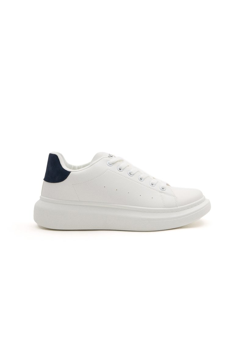 Zapatilla blanca de cuero con detalle azul marino en el talón, punta redonda, cierre de cordones, suela de plataforma y pequeños orificios para ventilación.