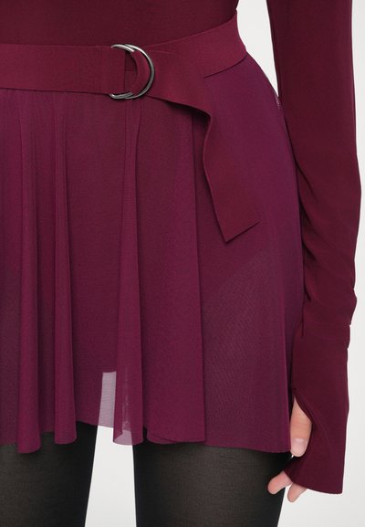 Vīnsarkanā kleita ar pieguļošu augšdaļu, garām piedurknēm un krojētu svārku daļu. Ir piemērots jostai ar sudraba metāla sprādzi. Daļēji caurspīdīga auduma.